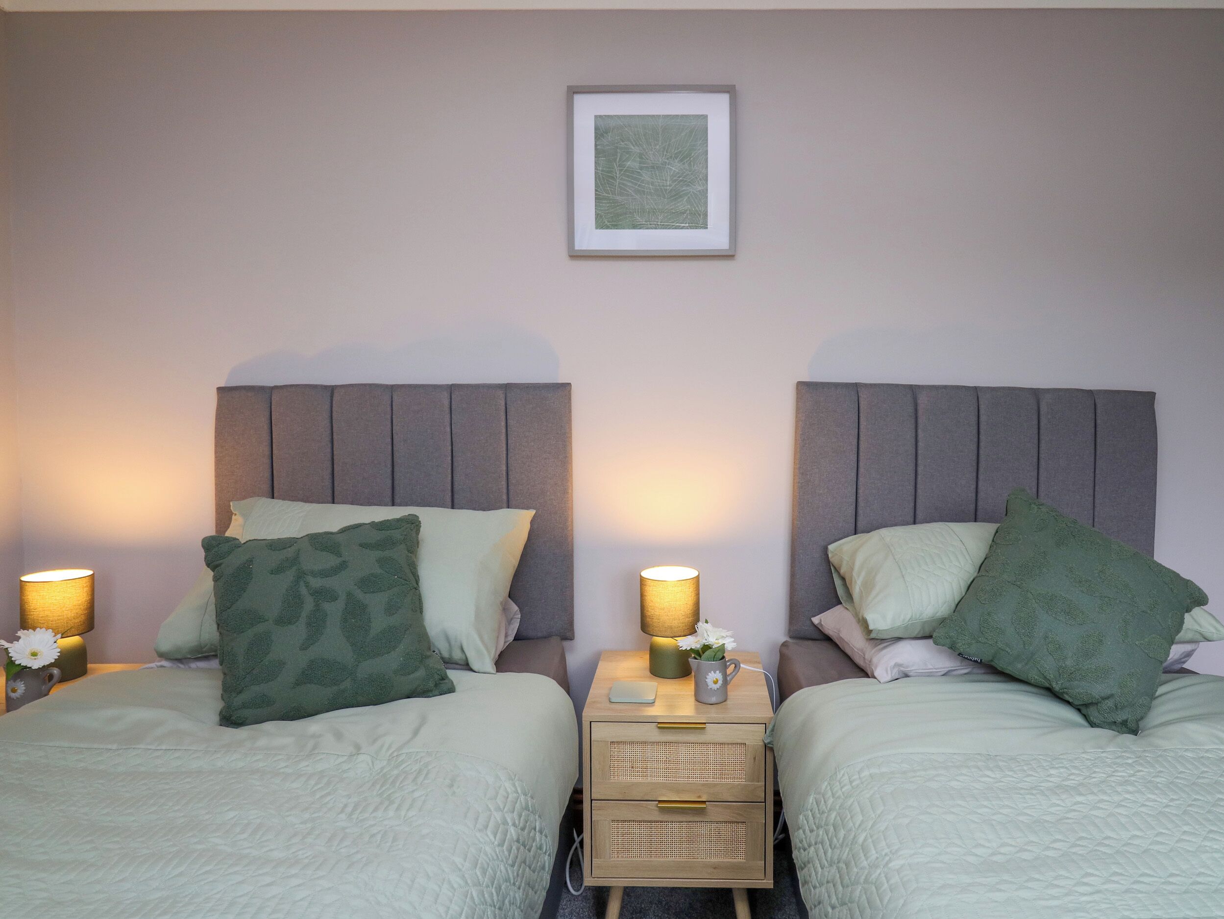 A twin room with two beds, each with a headboard, bedside tables with lamps, and a framed picture on the wall.