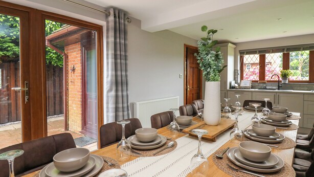 A dining area with a long wooden table set for a meal, surrounded by brown leather chairs.