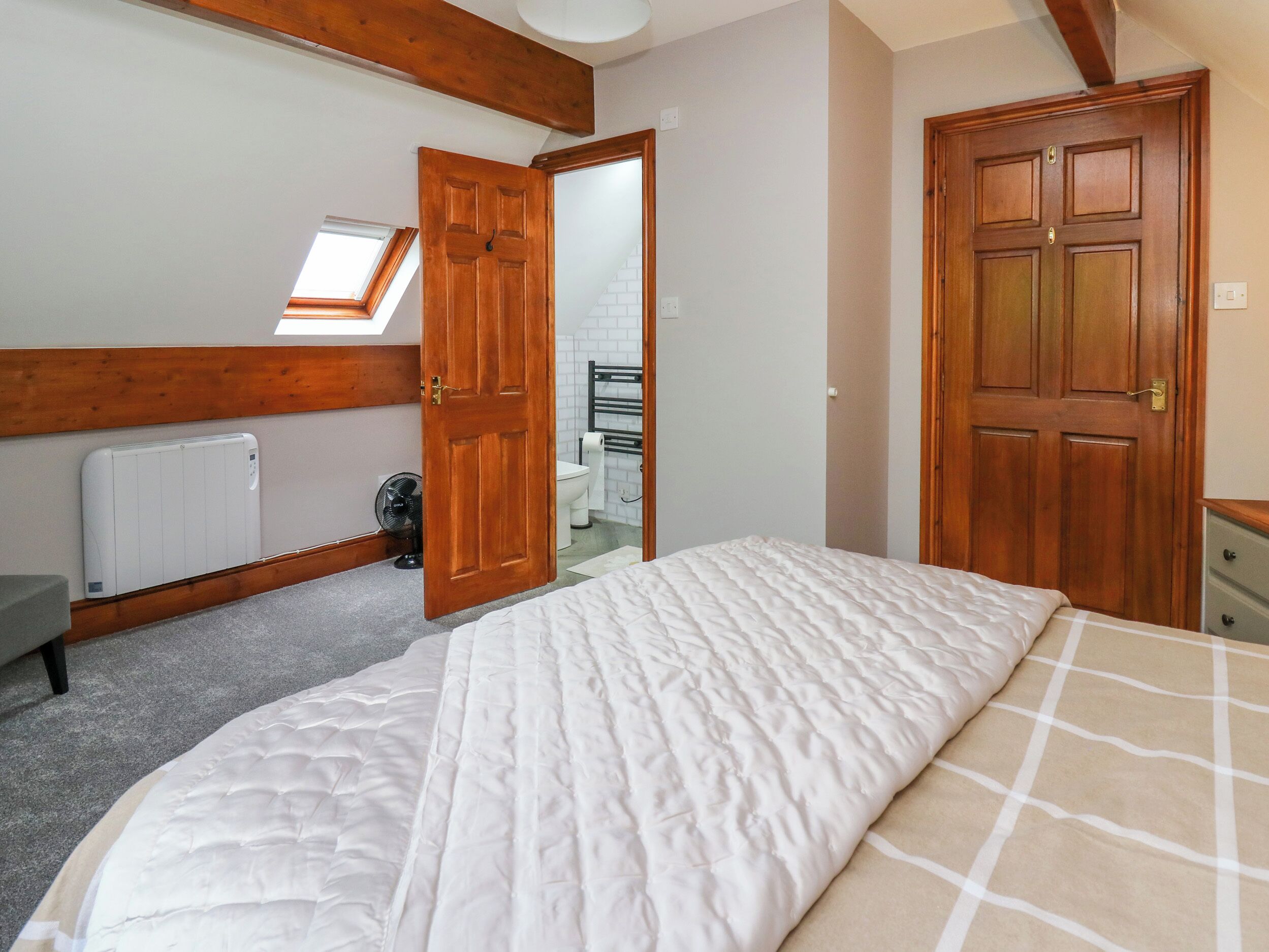 A bedroom with a bed, a radiator, a fan, a wooden door, and a skylight.