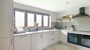 A modern kitchen with white cabinetry, a black stove, and a window with blinds.