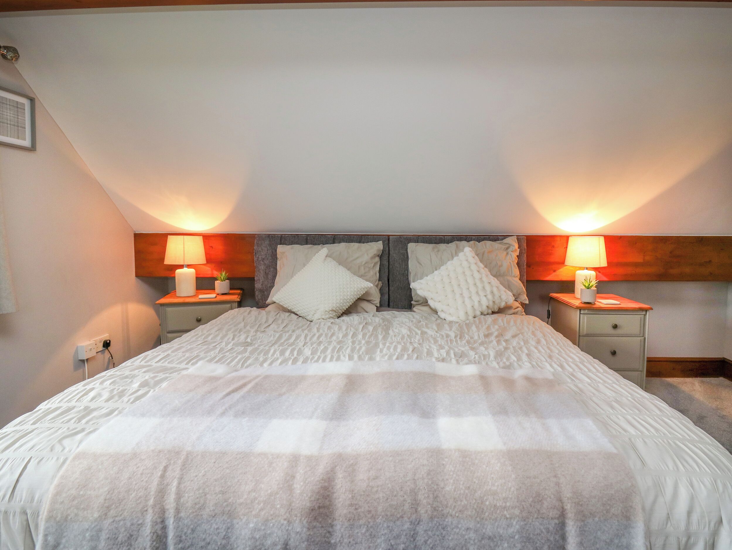 Ein Schlafzimmer mit einem großen Bett, zwei Nachttischen inklusive Lampen und einem hölzernen Kopfteil.