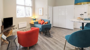Un salon moderne avec un canapé bleu, un fauteuil rouge, une petite table ronde et un téléviseur.