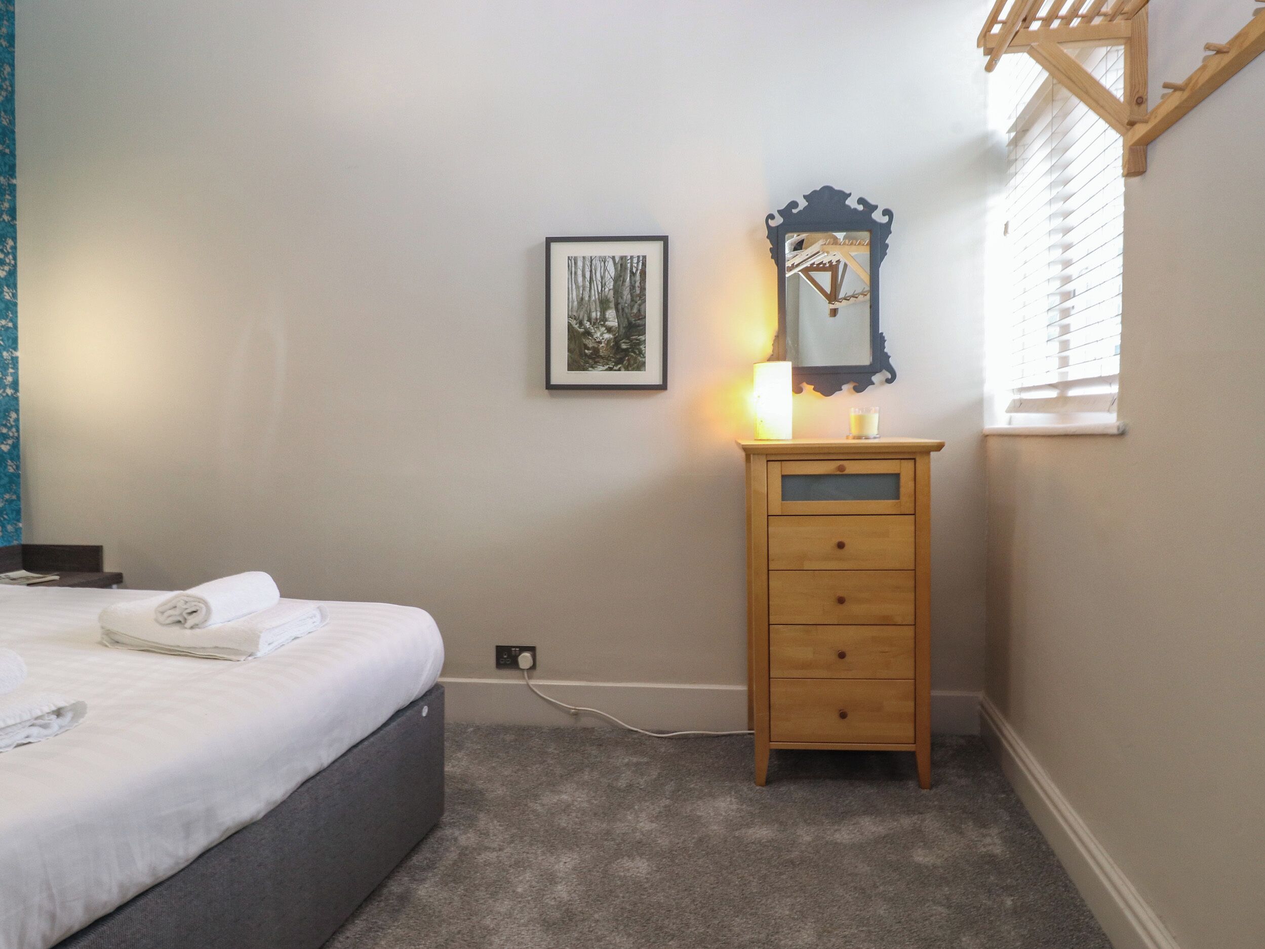 A bedroom with a bed, a wooden dresser, a framed picture, and a window with blinds.
