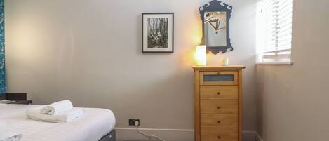 A bedroom with a bed, a wooden dresser, a framed picture, and a window with blinds.