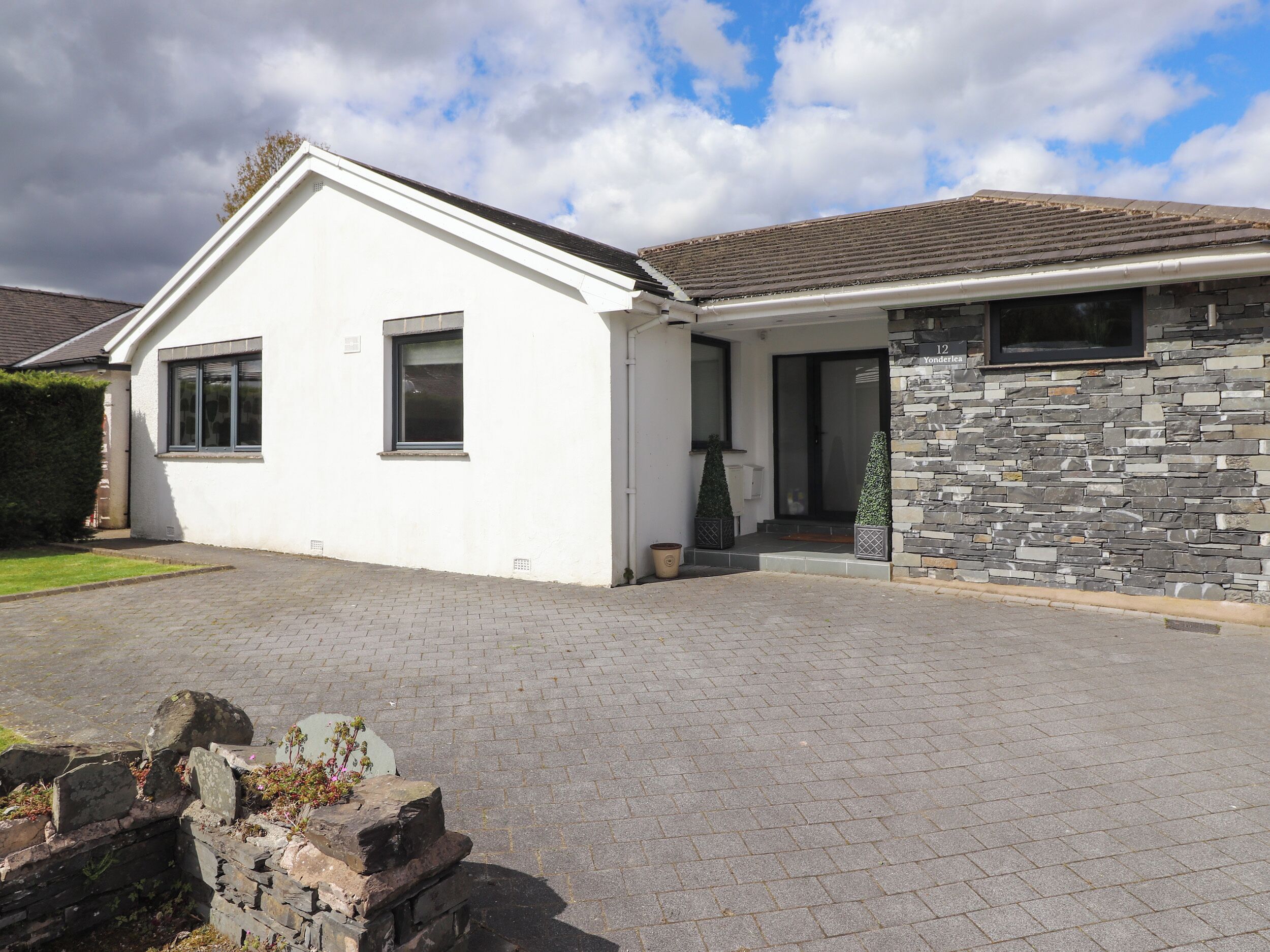 A single-story house with a white exterior, stone facade, and a paved driveway.