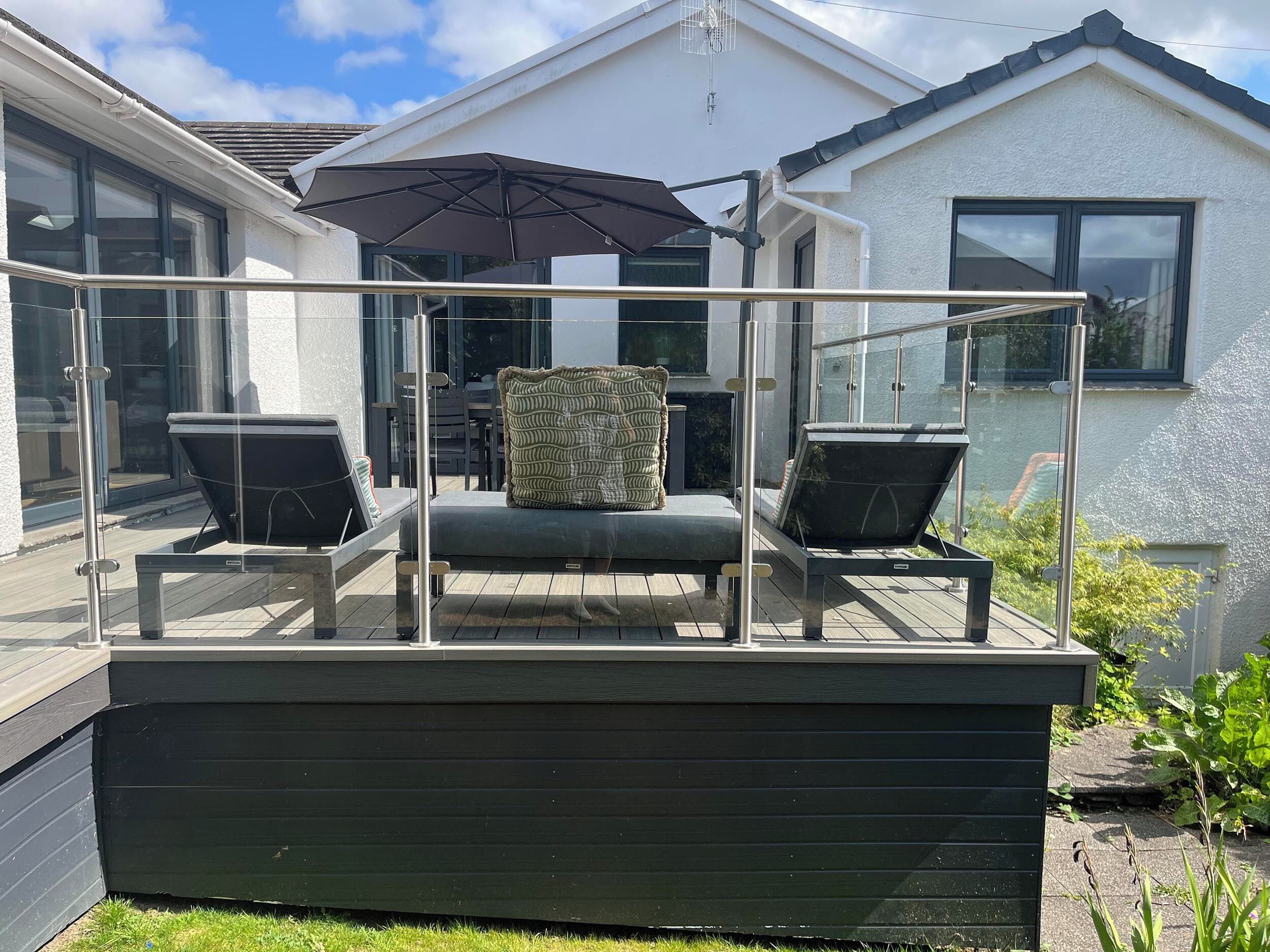A covered outdoor seating area with a glass railing, a cushioned bench, and a patterned throw pillow.
