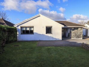 A single-story house with a sloped roof, a stone wall entrance, and a well-maintained lawn. - Yonder Lea (Windermere)