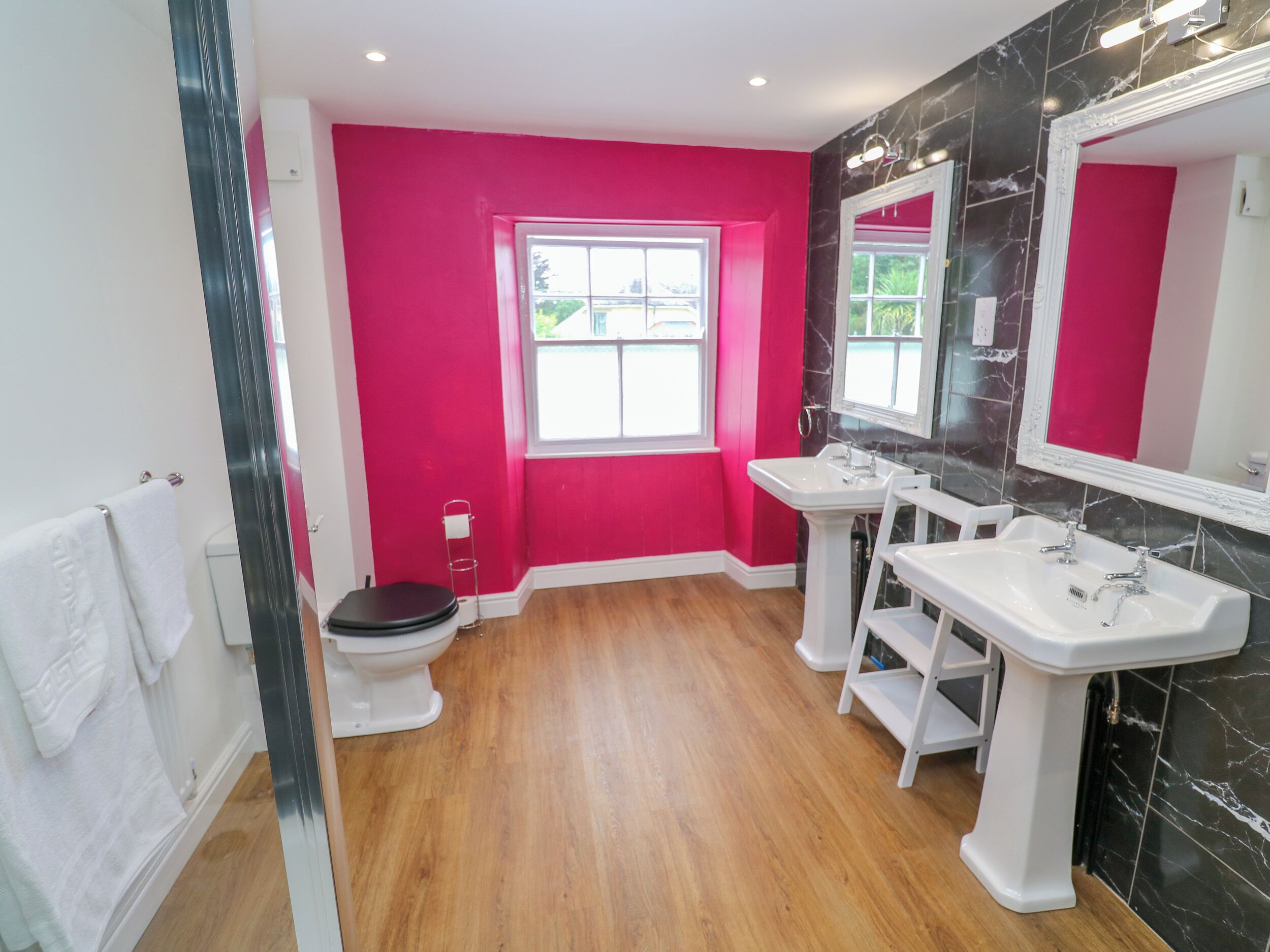 Une salle de bain avec un mur rose, des toilettes blanches, un lavabo blanc et un miroir.