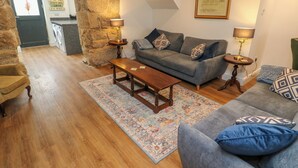A cozy living room with a stone wall, a grey sofa, a wooden coffee table, and a patterned rug.