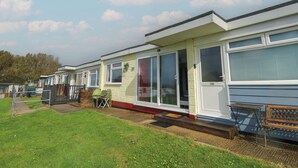 A row of mobile homes with large windows and sliding doors, a grassy lawn, and a wooden bench.