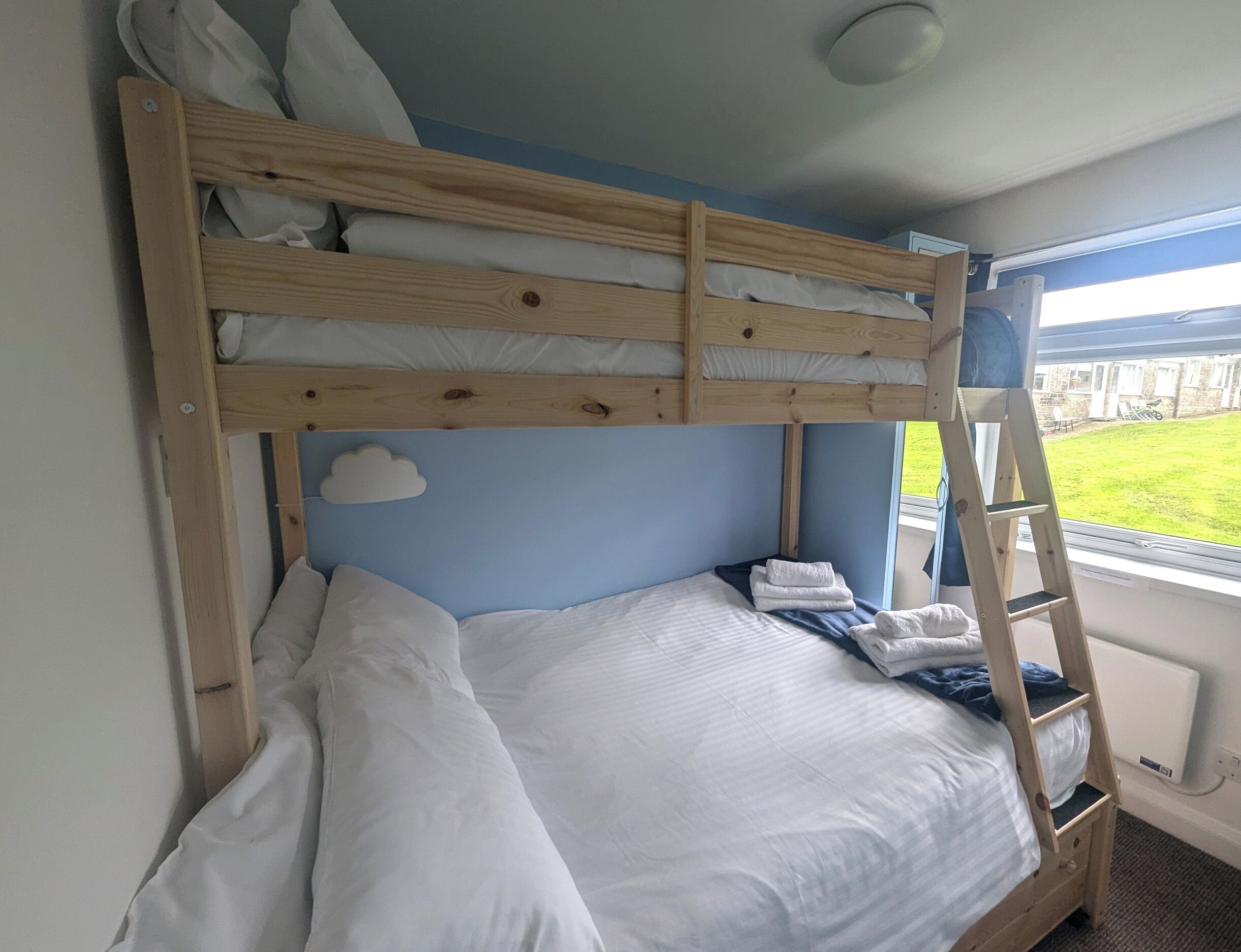 Una cama litera con estructura de madera, ropa de cama blanca y un adorno de nube en la pared.
