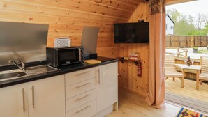A compact kitchen with a microwave, toaster, and sink. A flat-screen TV is mounted on the wall. - The Poddy (Swindon)