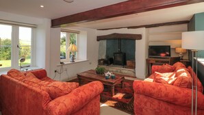 A living room with two red upholstered sofas, a wooden coffee table, a fireplace, and a television. - Brook Cottage (Sturminster Newton)