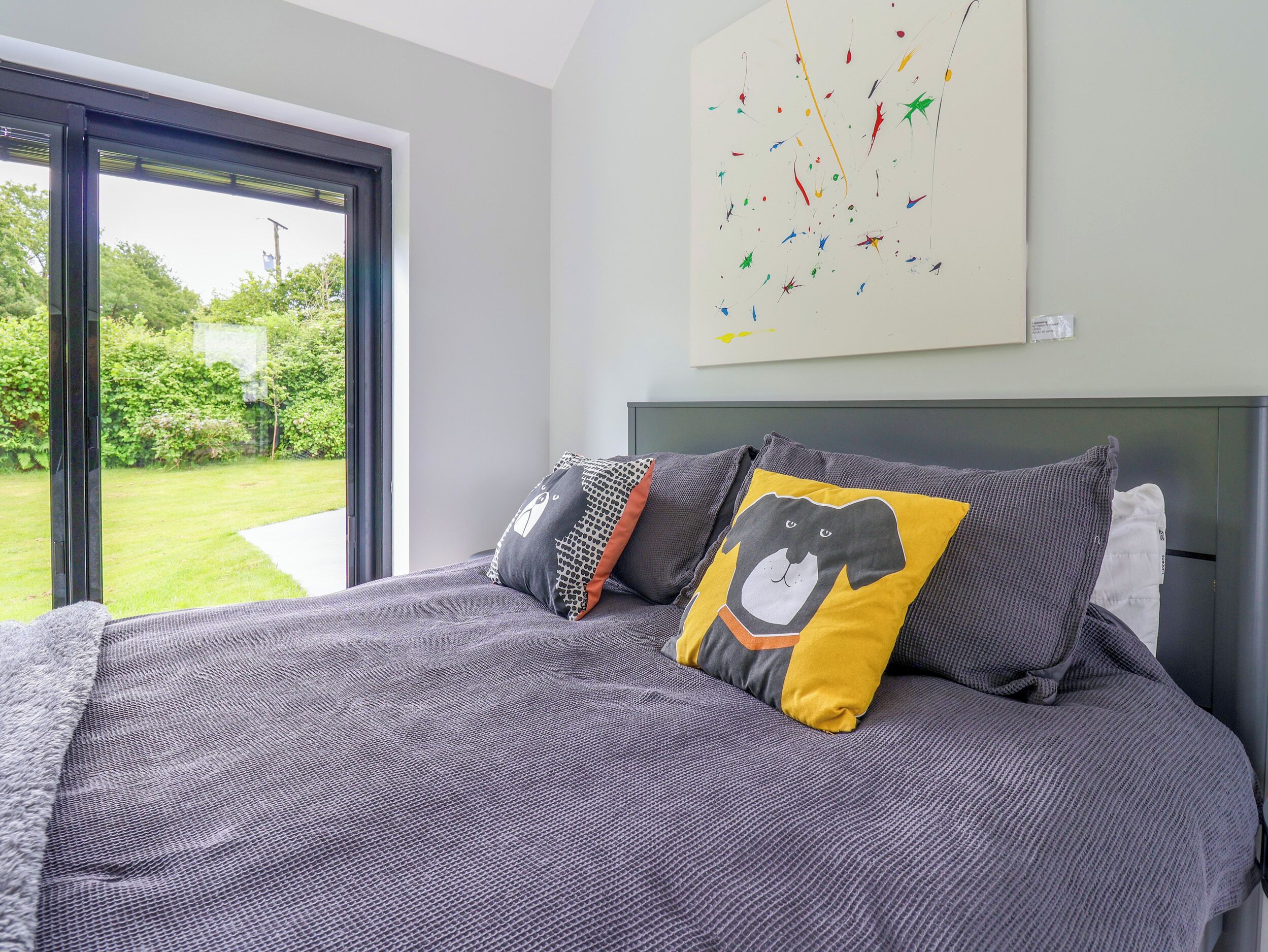 Una camera da letto moderna con un letto grande, vista sull'esterno attraverso una porta scorrevole e un quadro astratto colorato appeso alla parete.
