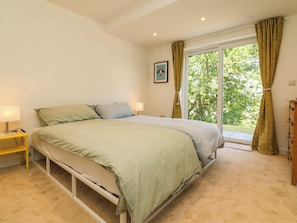 Un dormitorio con cama, lámparas de noche, ventana con cortinas y un cuadro en la pared.