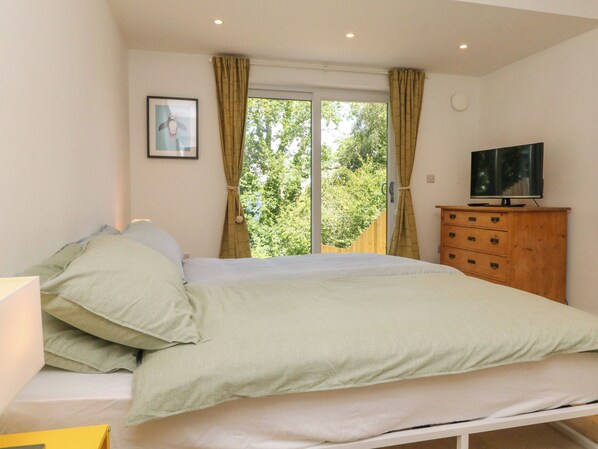 Un dormitorio con una cama, un aparador de madera, un televisor y una ventana con cortinas.