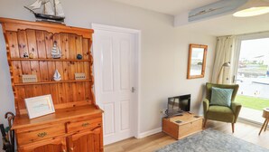 Una habitación con un armario de madera, un televisor sobre un mueble de madera, un sillón verde y vistas a un cuerpo de agua por una ventana.