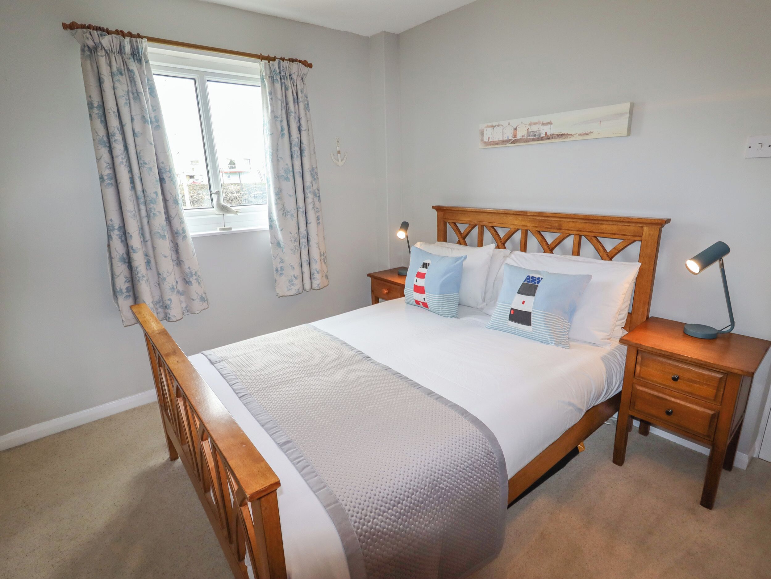 A neatly made bed with a wooden headboard, two bedside tables with lamps, and a window with curtains.