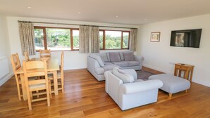 A spacious living area with a dining table, grey sofas, and a wooden floor. - Little Owl Barn (Worcester)