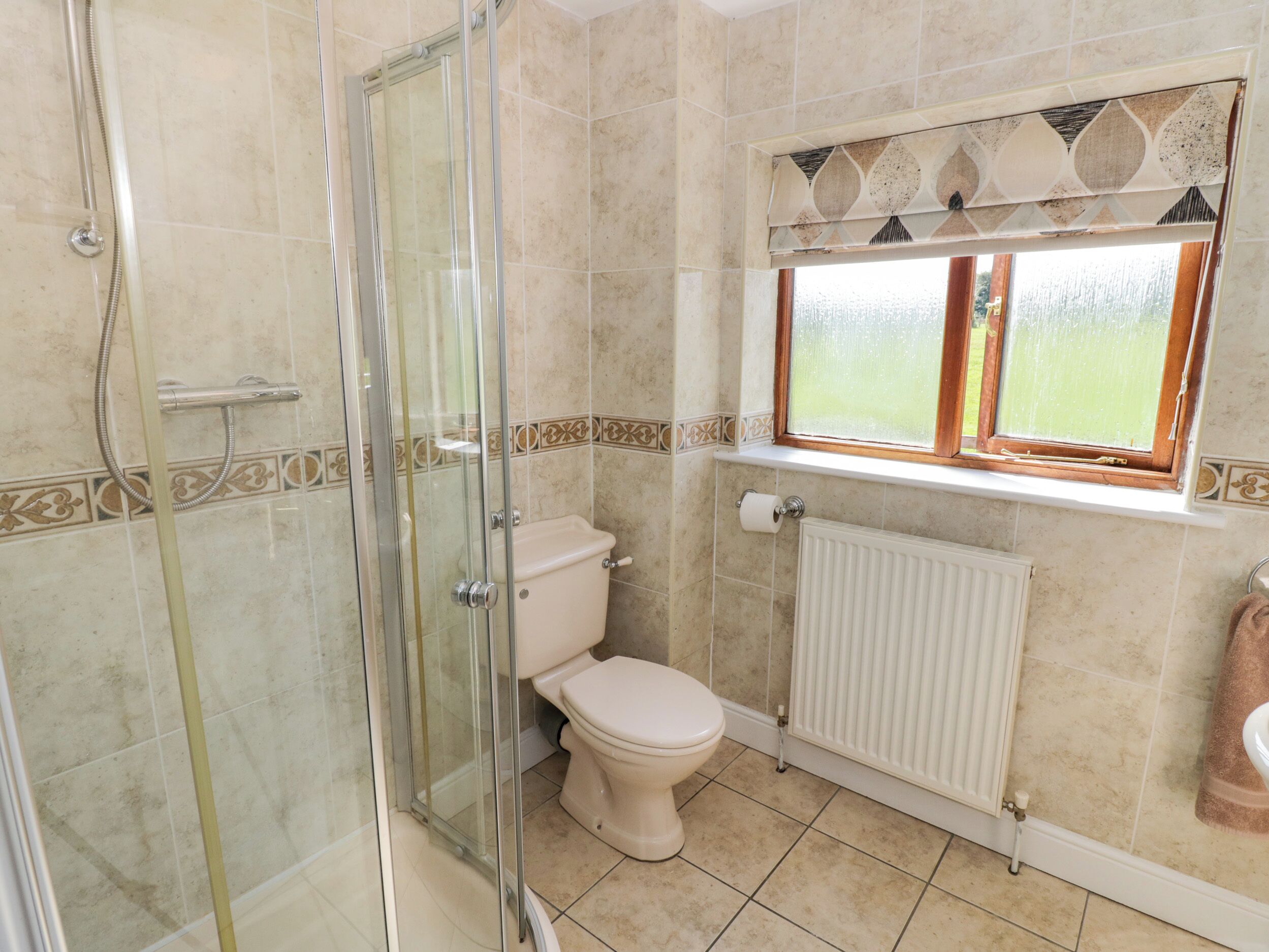 A bathroom with a glass-enclosed shower, a toilet, and a window with a view.