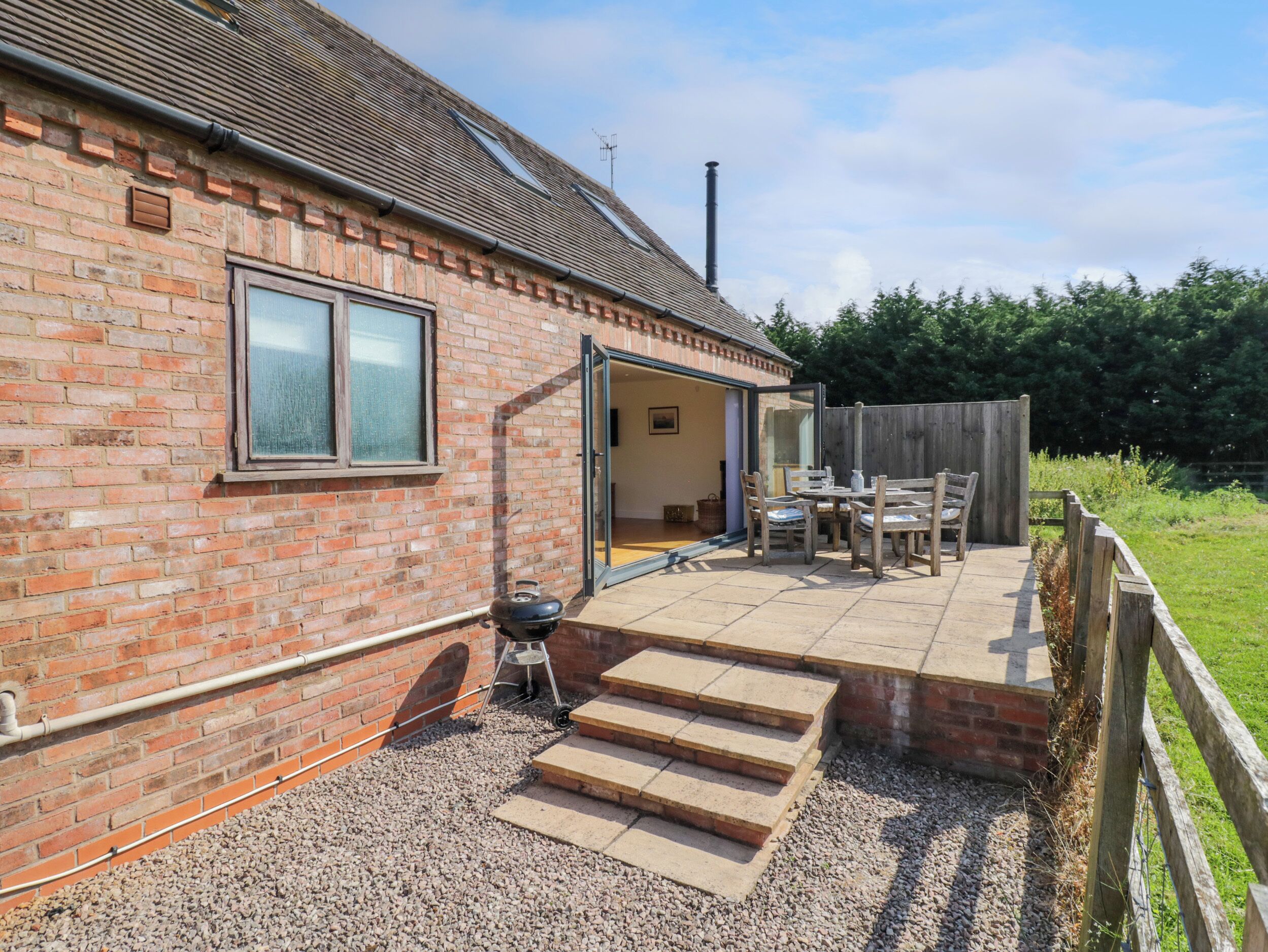 A brick house with a patio, a barbecue grill, and a wooden fence.