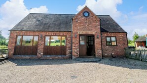A brick building with a gabled roof, large windows, and a circular skylight. - Little Owl Barn (Worcester)