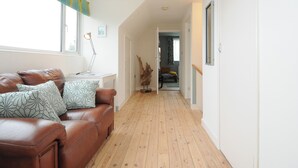A hallway with a brown leather sofa, a desk with a lamp, and a wooden floor. - Sea Drift (St Austell)