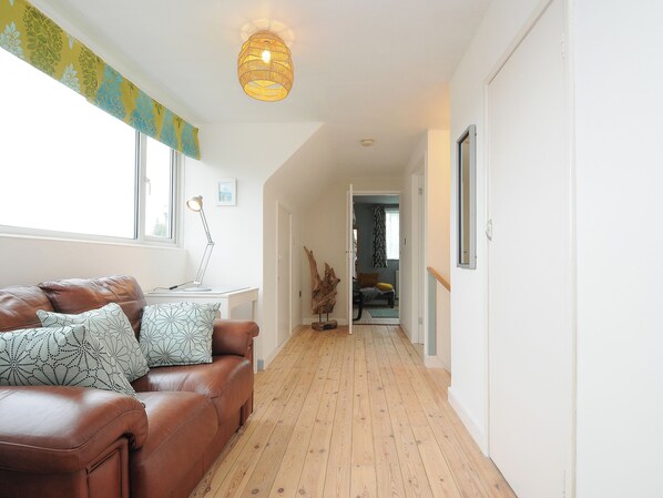 A hallway with a brown leather sofa, a desk with a lamp, and a wooden floor.