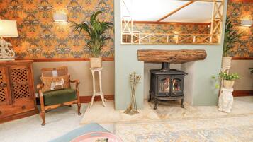 A cozy room with a wooden chair, a small table with a plant, a fireplace, and a patterned wallpaper.