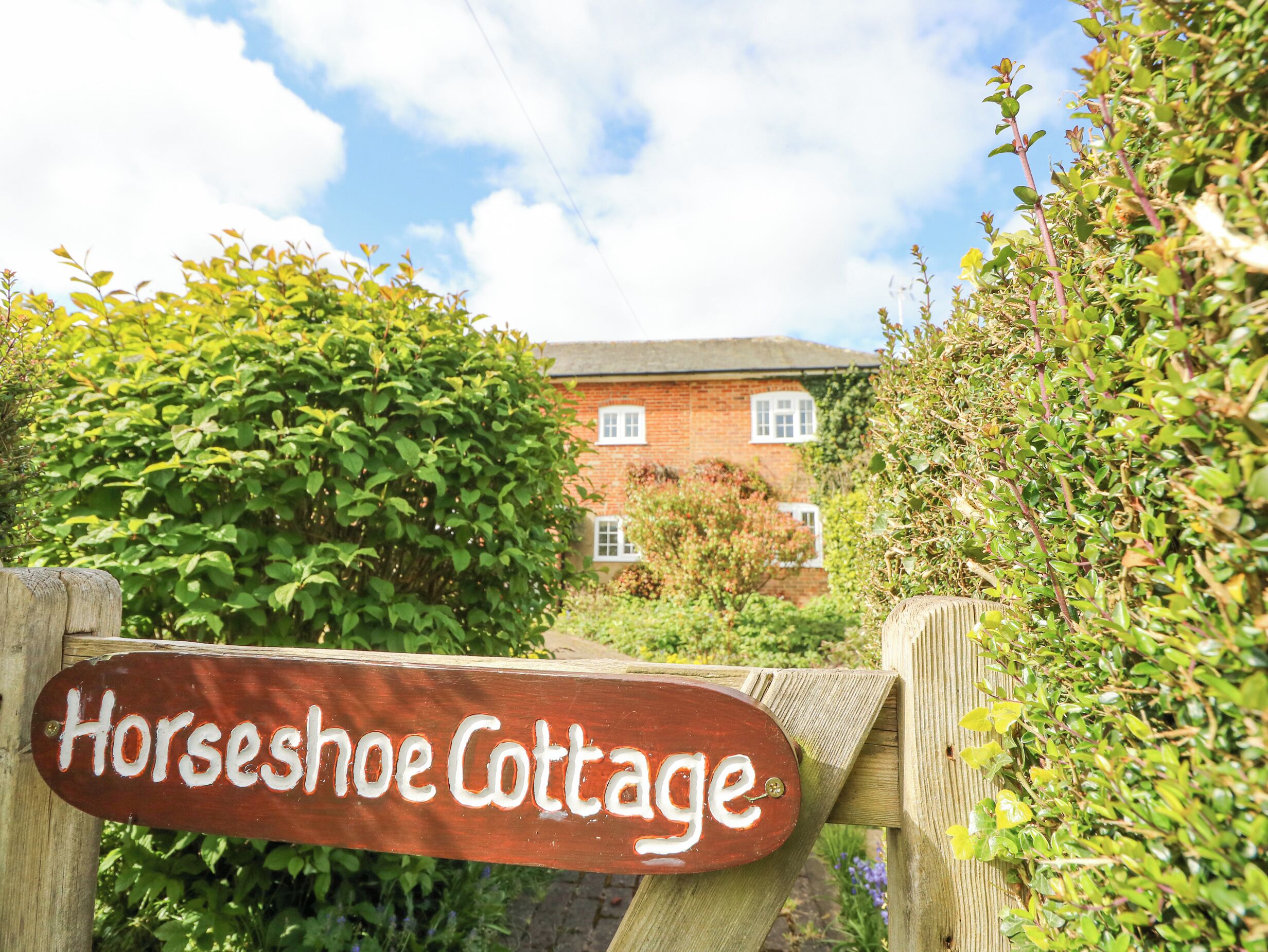 A wooden sign for Horseshoe Cottage with a brick building in the background.
