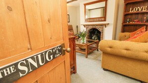 A cozy living room with a wooden door labeled "THE SNUG RELAY & CHILL," a fireplace, a sofa, and a bookshelf with the word "LOVE" on it. - Horseshoe Cottage (Romsey)