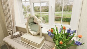 A bathroom with a window, a mirror, a vanity table, and a vase with flowers. - Horseshoe Cottage (Romsey)