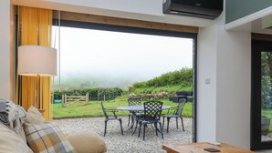 Una sala de estar moderna con un sofá, una mesa de centro de madera y vista a un jardín a través de un gran ventanal.