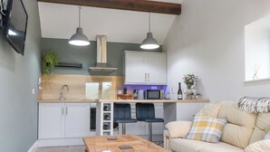 Un espacio habitable compacto con kitchenette, una mesa de comedor de madera, un sofá y un televisor montado en la pared.