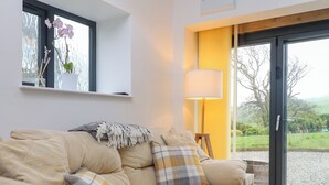 Un salón acogedor con un sofá color beige, una lámpara y vista a un jardín a través de un ventanal.