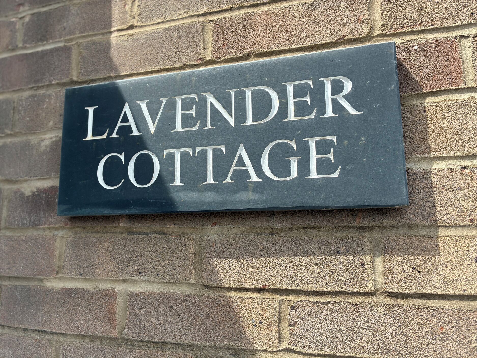 Een donkergrijs bord waarop in grote, witte letters 'LAVENDER COTTAGE' staat.