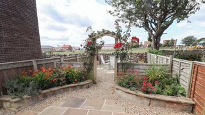 Un sendero en un jardín que conduce a un arco de madera, rodeado de macizos de flores y un patio empedrado.