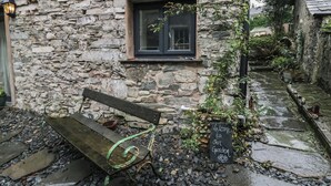 A stone building with a bench outside, a window, and a sign welcoming visitors to the garden. - Eden Vale Cart House (Broughton in Furness)