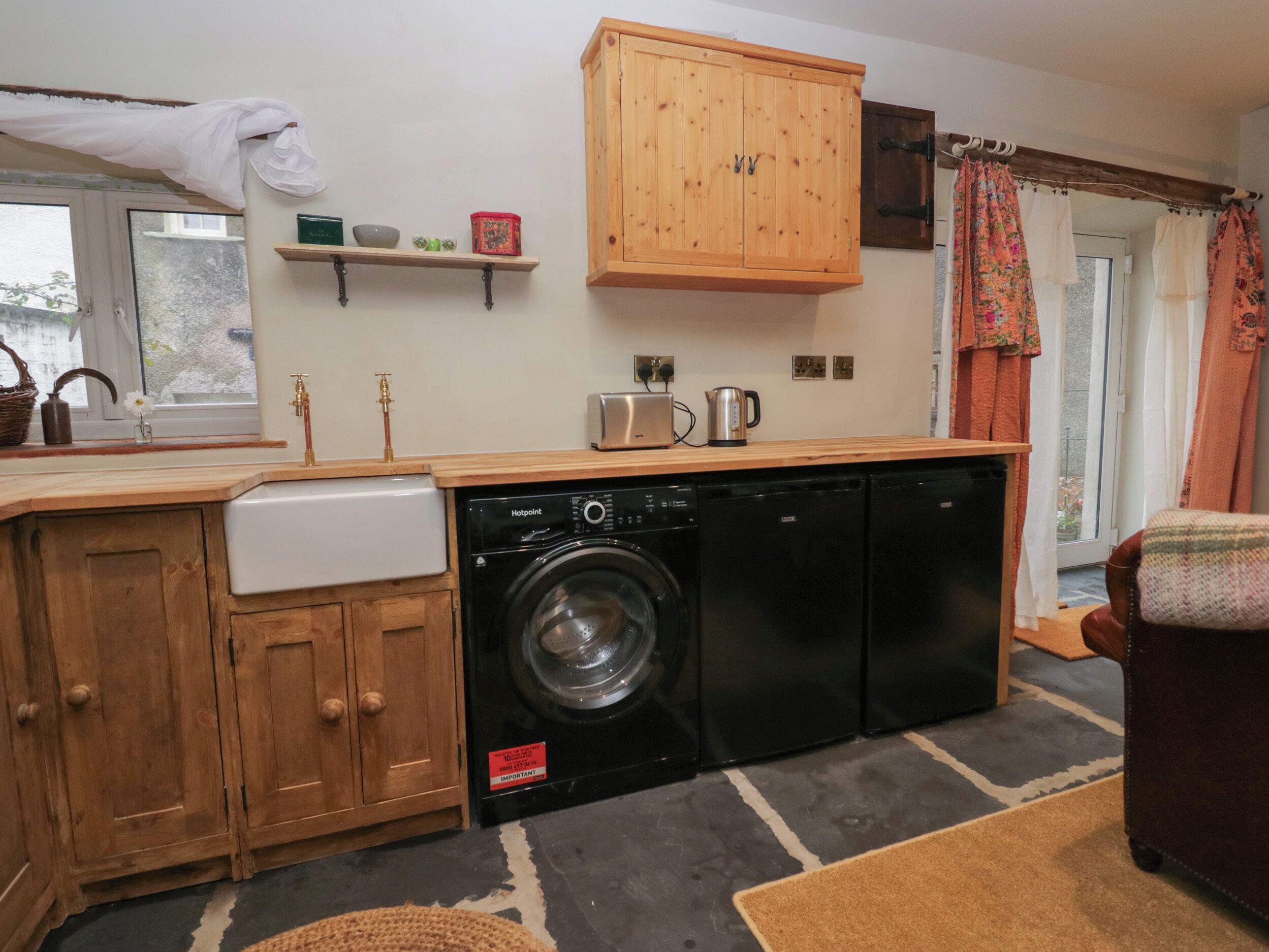 A compact kitchen with wooden cabinets, a washing machine, a dishwasher, and a small countertop with a toaster and kettle.