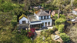 Ein modernes, zweistöckiges Haus mit einem großen Wintergarten, umgeben von üppiger Vegetation und einem Kiesweg.