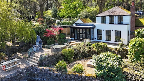 A modern house with a stone wall, a barbecue, and a garden with various plants.