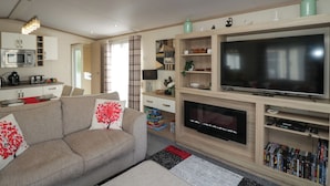 Ein modernes Wohnzimmer mit Flachbildfernseher, einer Couch, einem Kamin und einer Küche im Hintergrund.