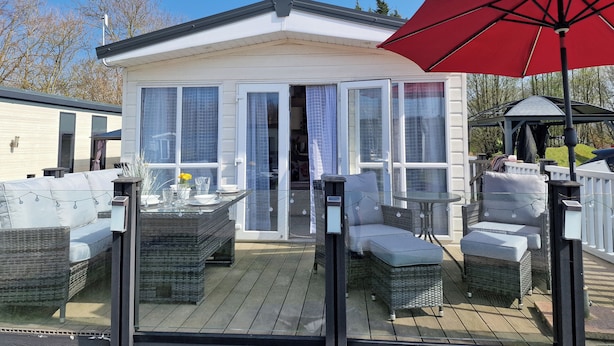 Ein überdachter Patio-Bereich mit Gartenmöbeln, einem Glastür-Eingang und einem roten Sonnenschirm.