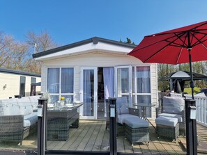 A covered patio area with outdoor furniture, a glass door entrance, and a red umbrella. - Ladybird Lodge (Carnforth)