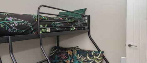Una cama litera con ropa de cama estampada en motivos florales en una habitación con una puerta blanca y un enchufe en la pared.