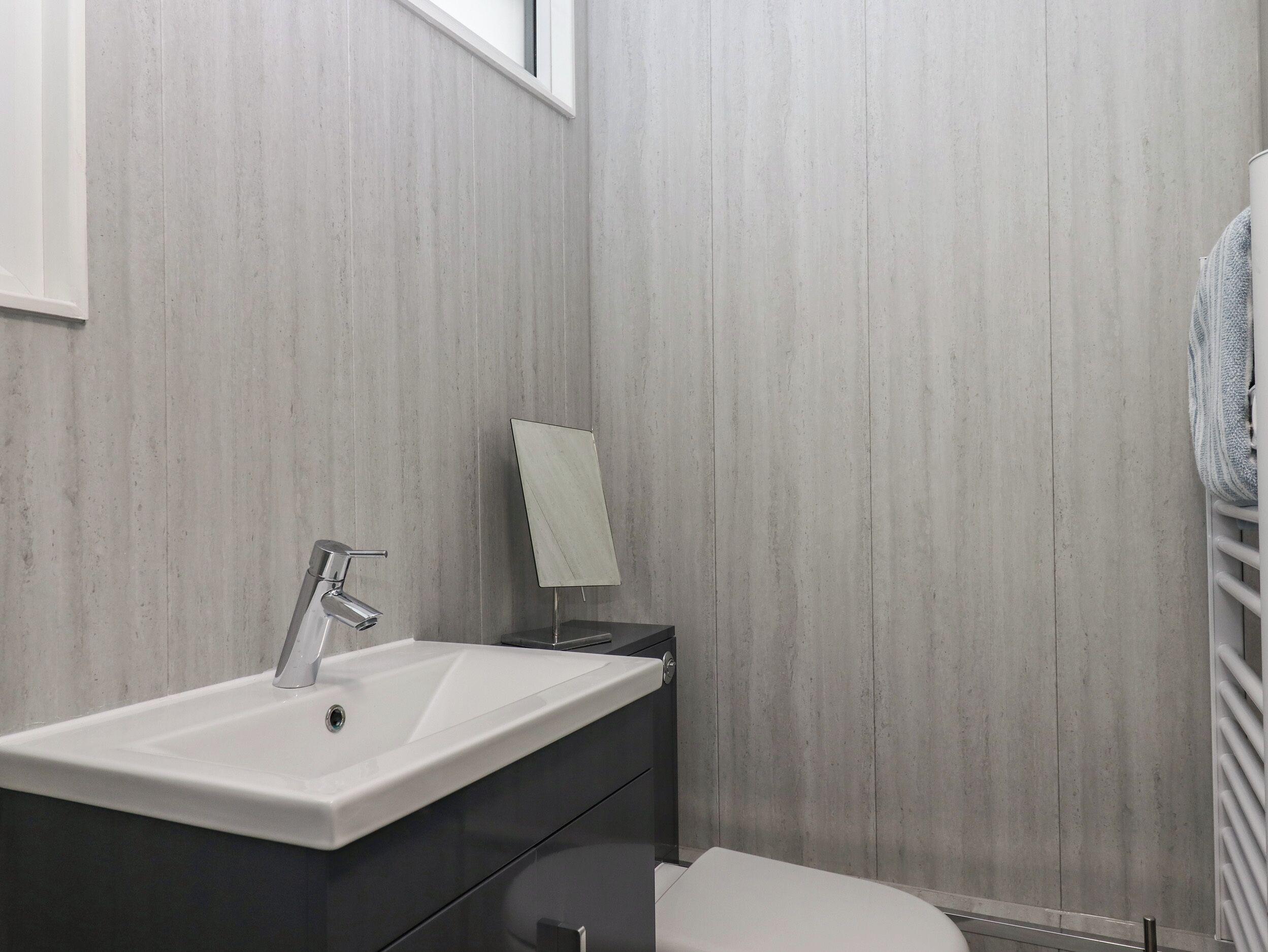 A modern bathroom with a white sink, dark cabinetry, a towel hanging on the wall, and a toilet.
