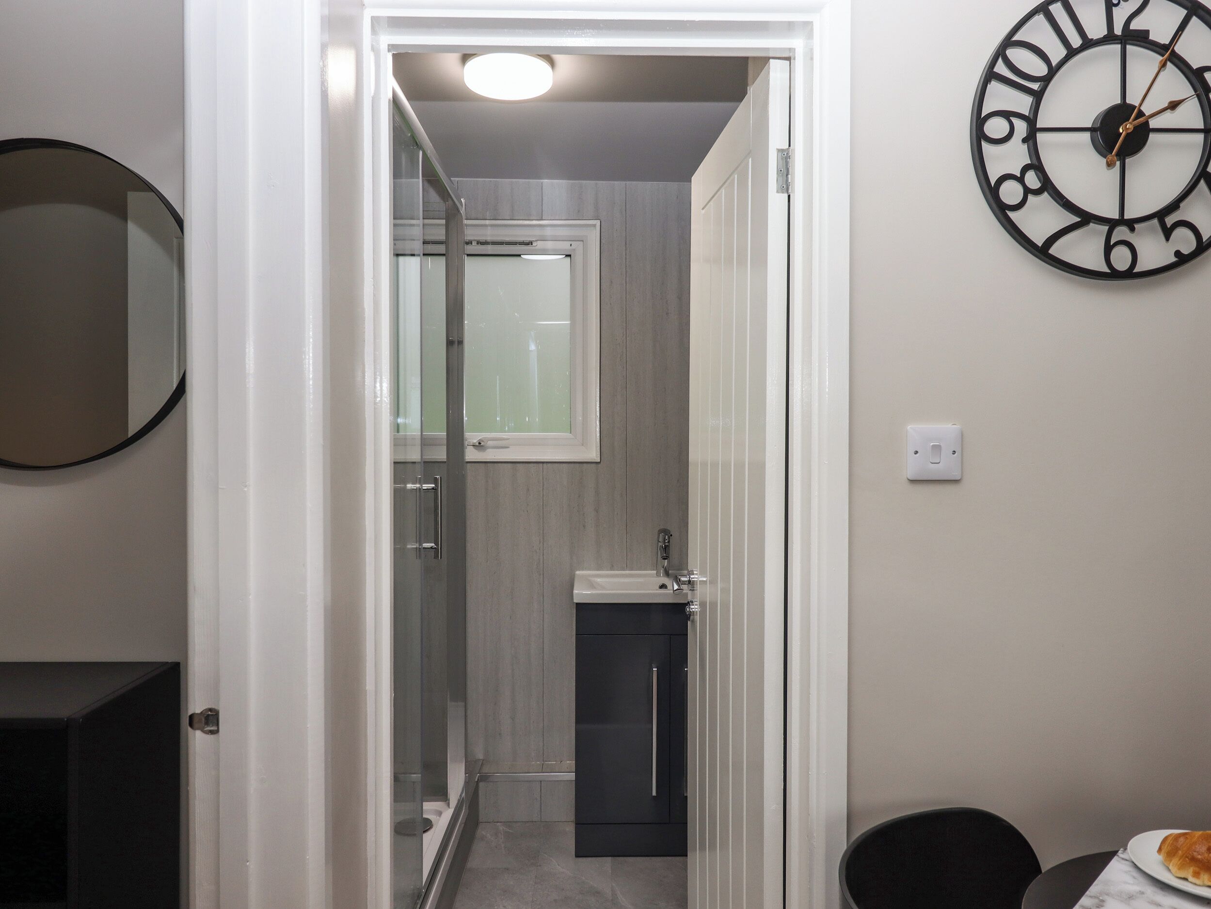 Une salle de bain avec une porte de douche en verre, un lavabo et une horloge au mur.