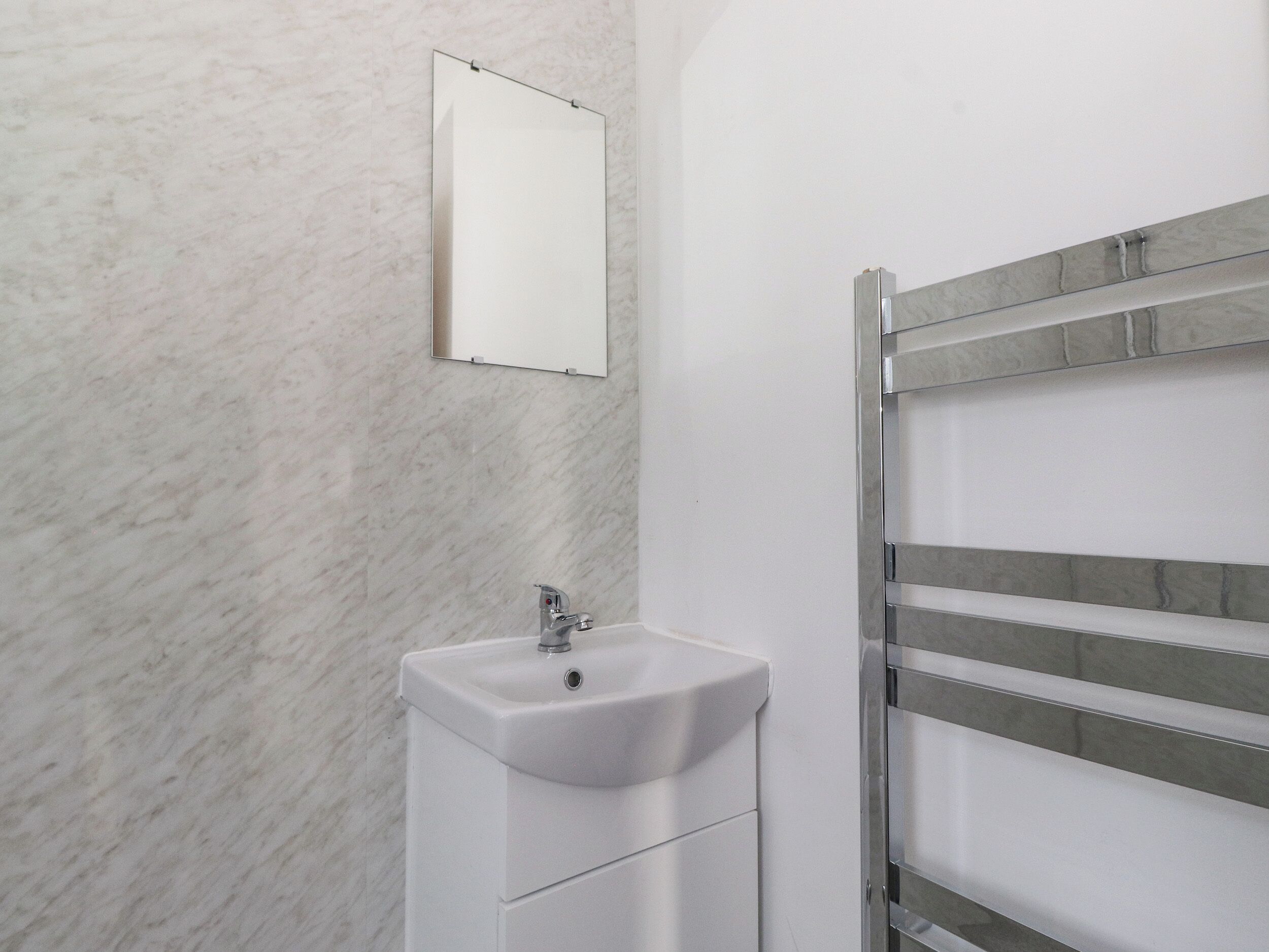 Un baño con un lavabo blanco, un espejo y un perchero para toallas.