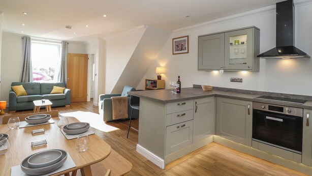 A modern kitchen with grey cabinets, a built-in oven, and a dining area with a table set for four. - 2 South Street (Wigton)