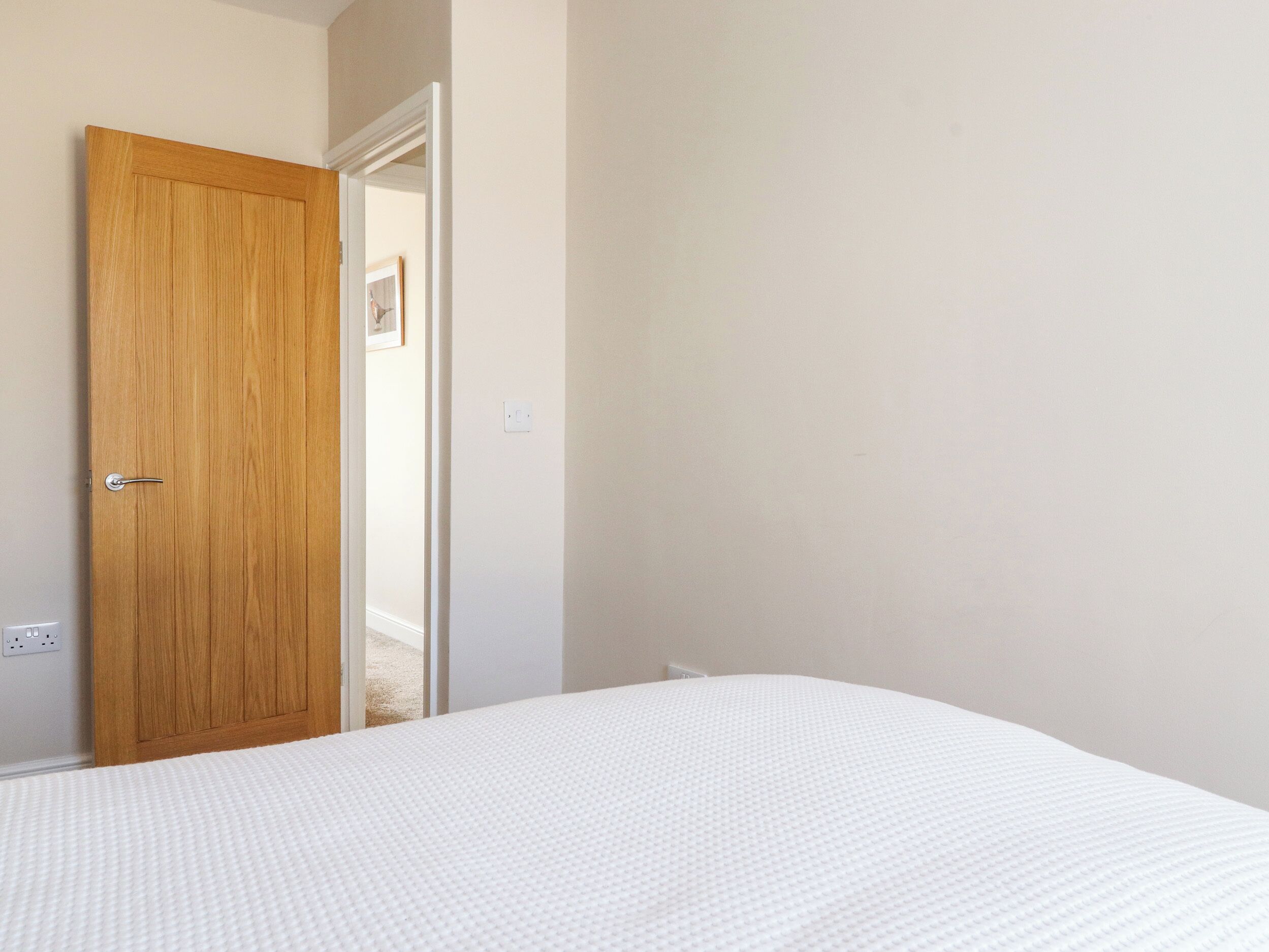 A bedroom with a wooden door, a white bed, and a white wall.